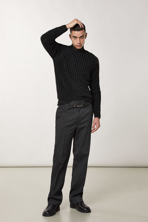 A male model wearing a long-sleeved black ribbedPatrizia Pepe sweater with a round neckline, paired with dark trousers and black shoes.
