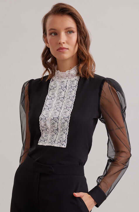 The EPOPEE is a black jersey pullover top with a center ribbon appliqué front made of a triple lace rose column that extends to create a mock neck. The pleated shoulders give way to a voluminous sheer sleeve that are finished with black jersey single French cuffs that allow for cufflinks. The EPOPEE features a hidden zipper at the back for closure.