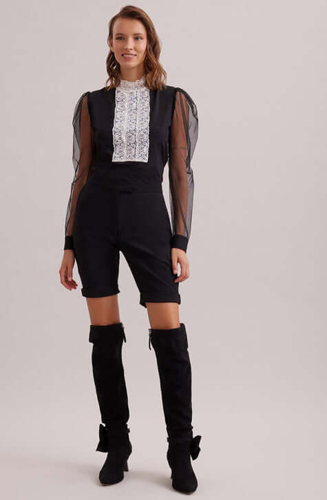 The EPOPEE is a black jersey pullover top with a center ribbon appliqué front made of a triple lace rose column that extends to create a mock neck. The pleated shoulders give way to a voluminous sheer sleeve that are finished with black jersey single French cuffs that allow for cufflinks. The EPOPEE features a hidden zipper at the back for closure.